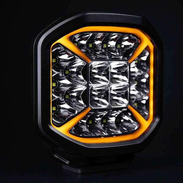 Strands Siberia X 7" lisävalo upealla oranssilla kehäparkilla joka kiertää valaisimen reunat ja kulmat tulevat keskikohtaa kohden muduostaen X kuvion. Valo on 8 kulmainen suorakaide. Mustalla taustalla.