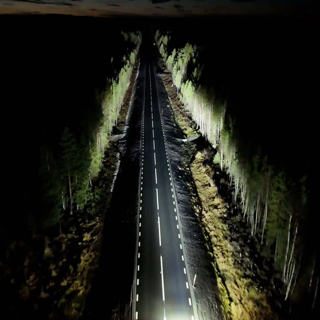 Ilmakuva pimeästä maantiestä, jota voimakas ja pitkä valokeila valaisee metsän keskellä.